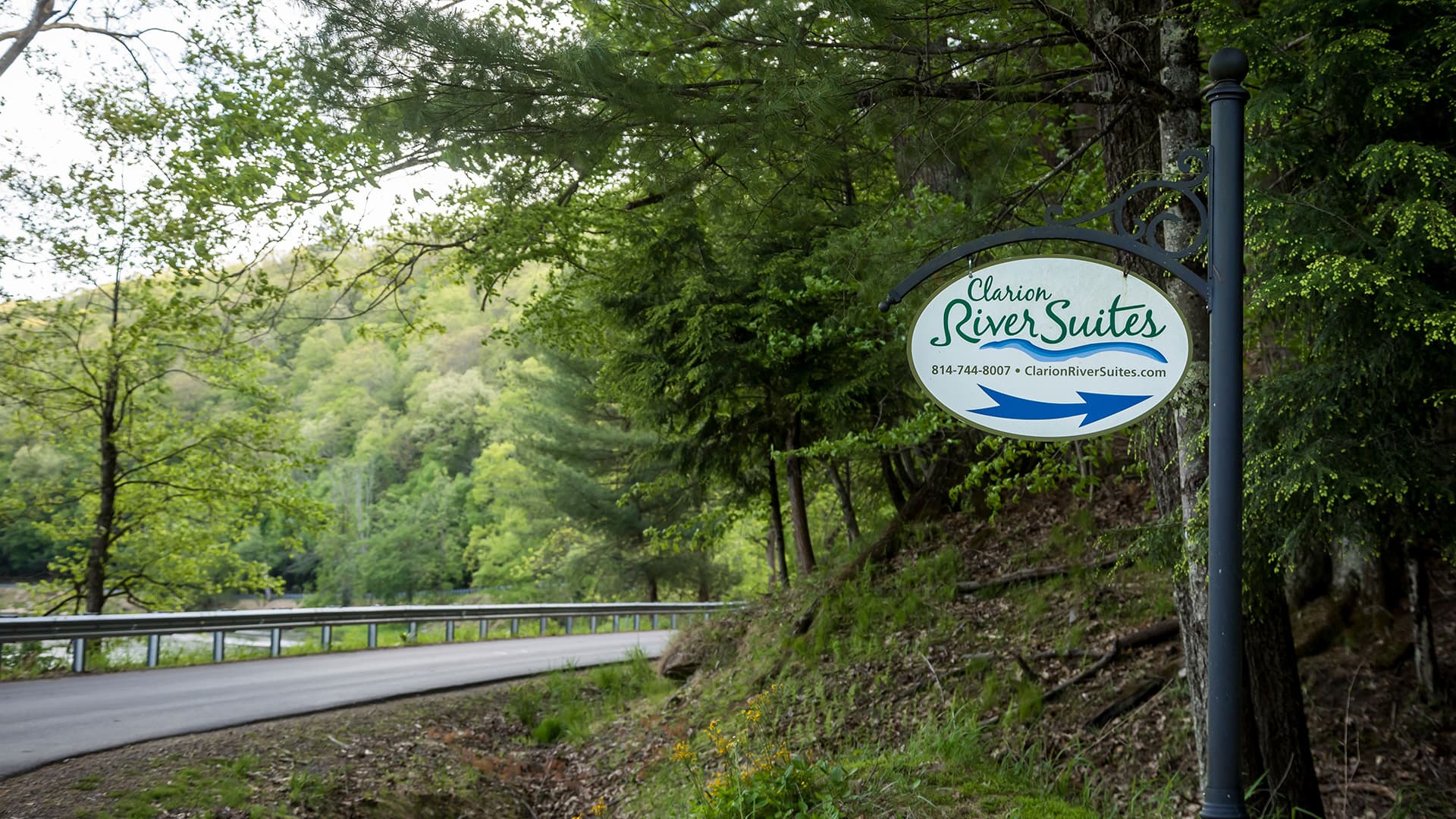 Sign for Clarion River Suites directing visitors along a scenic road surrounded by greenery.
